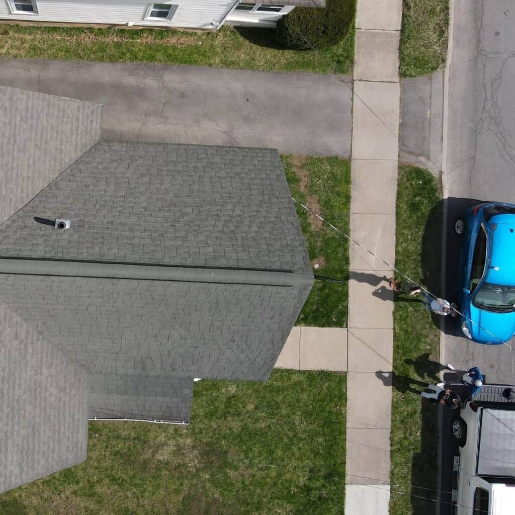 Aerial view of a house with sidewalk and parked cars in a neighborhood.
